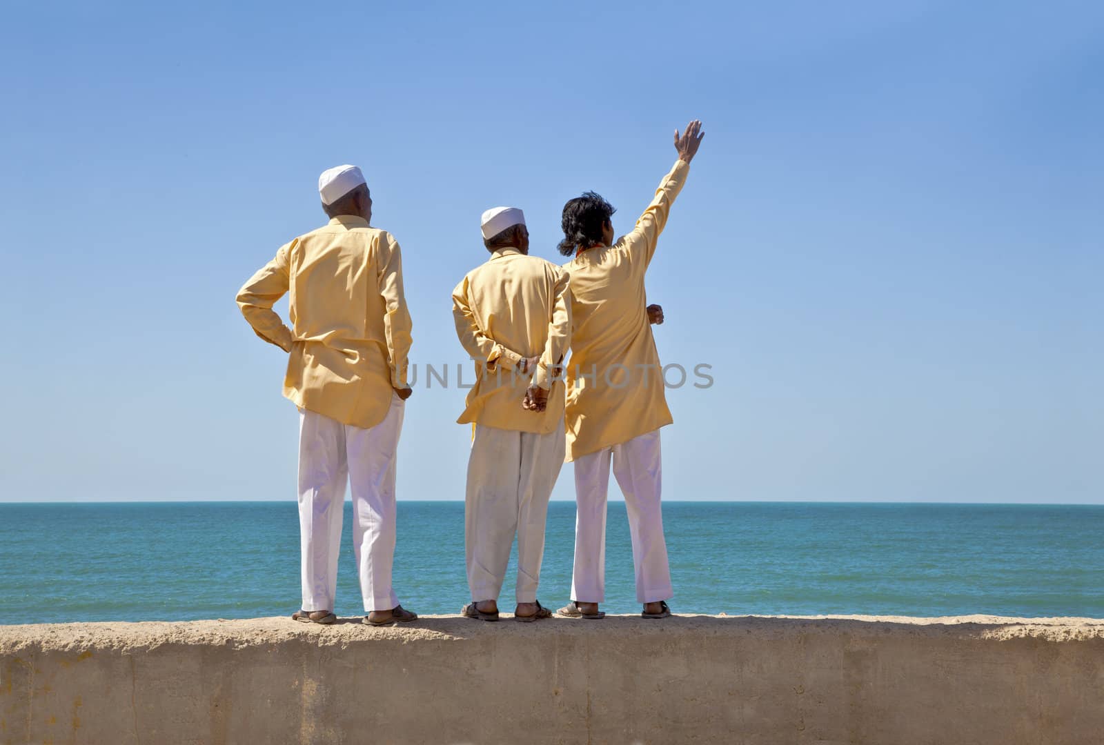 Horizontal portrait of three clerics in formal attire looking and pointing out to the horizon of the Arabian Sea. The location of this conceptual shot was at the beach of Dwarka Bay, Gujarat, India near the Krishna Temple.