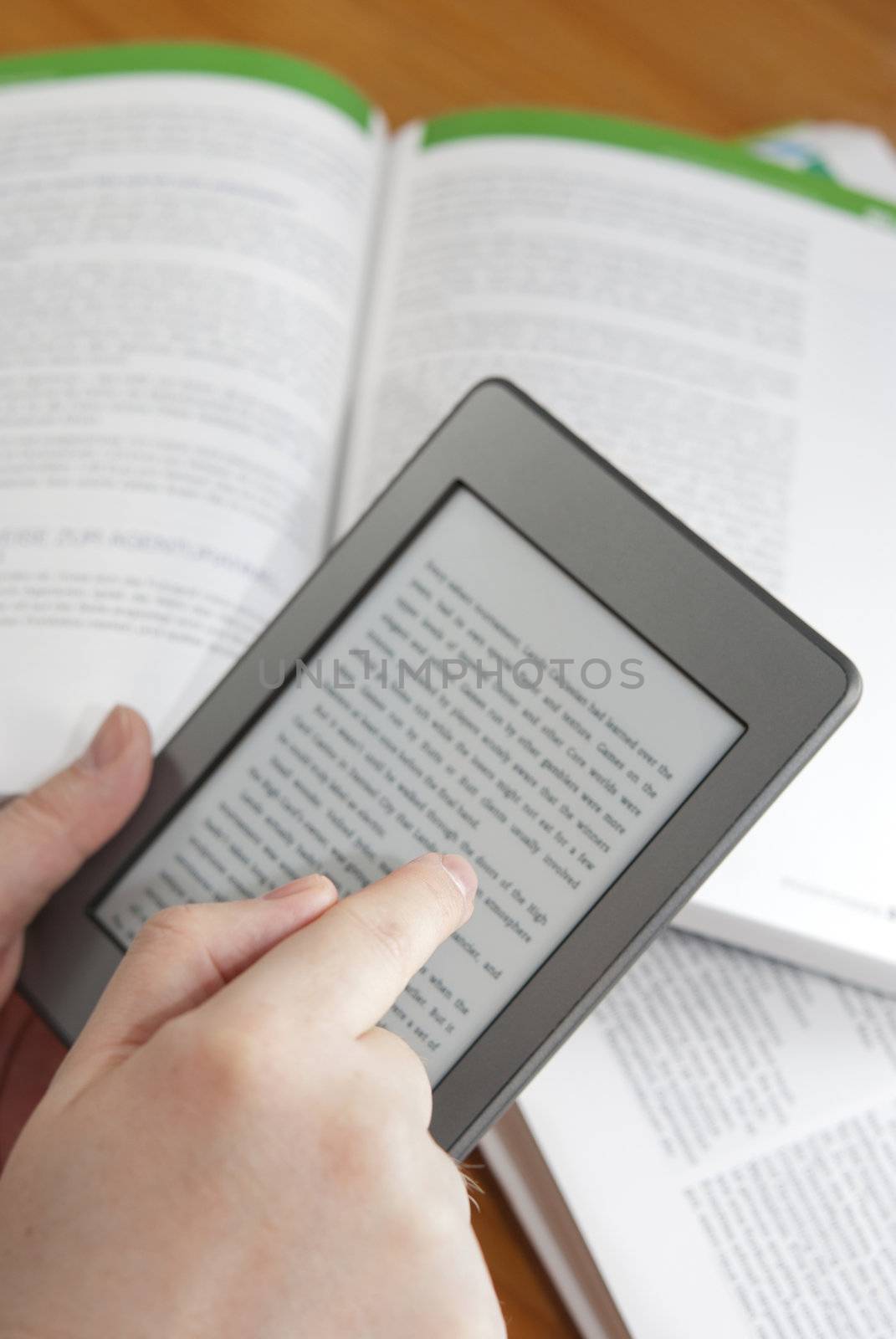 Man hands holding  an electronic book reader with text on the screen, open books in the background