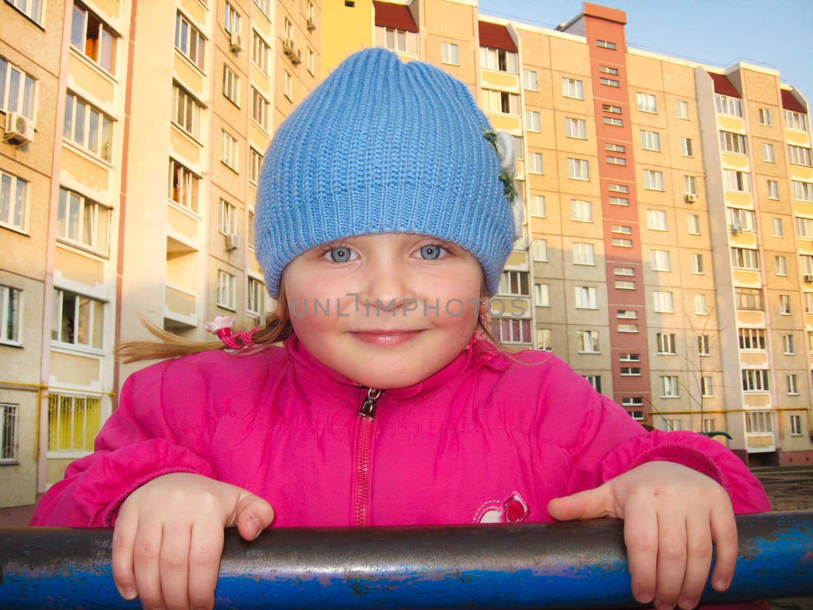The blue-eyed girl on a horizontal bar on a background of the multi-storey house