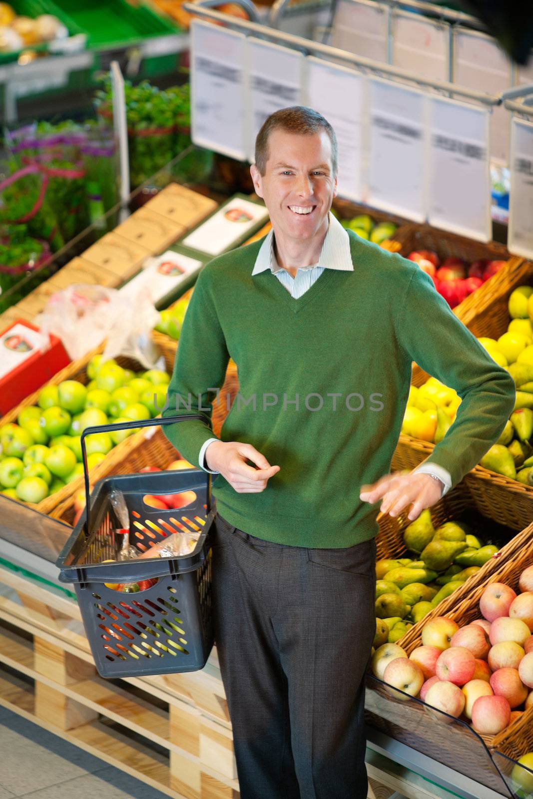 Mid adult man carrying shopping basket and looking at camera while shopping in fruit store