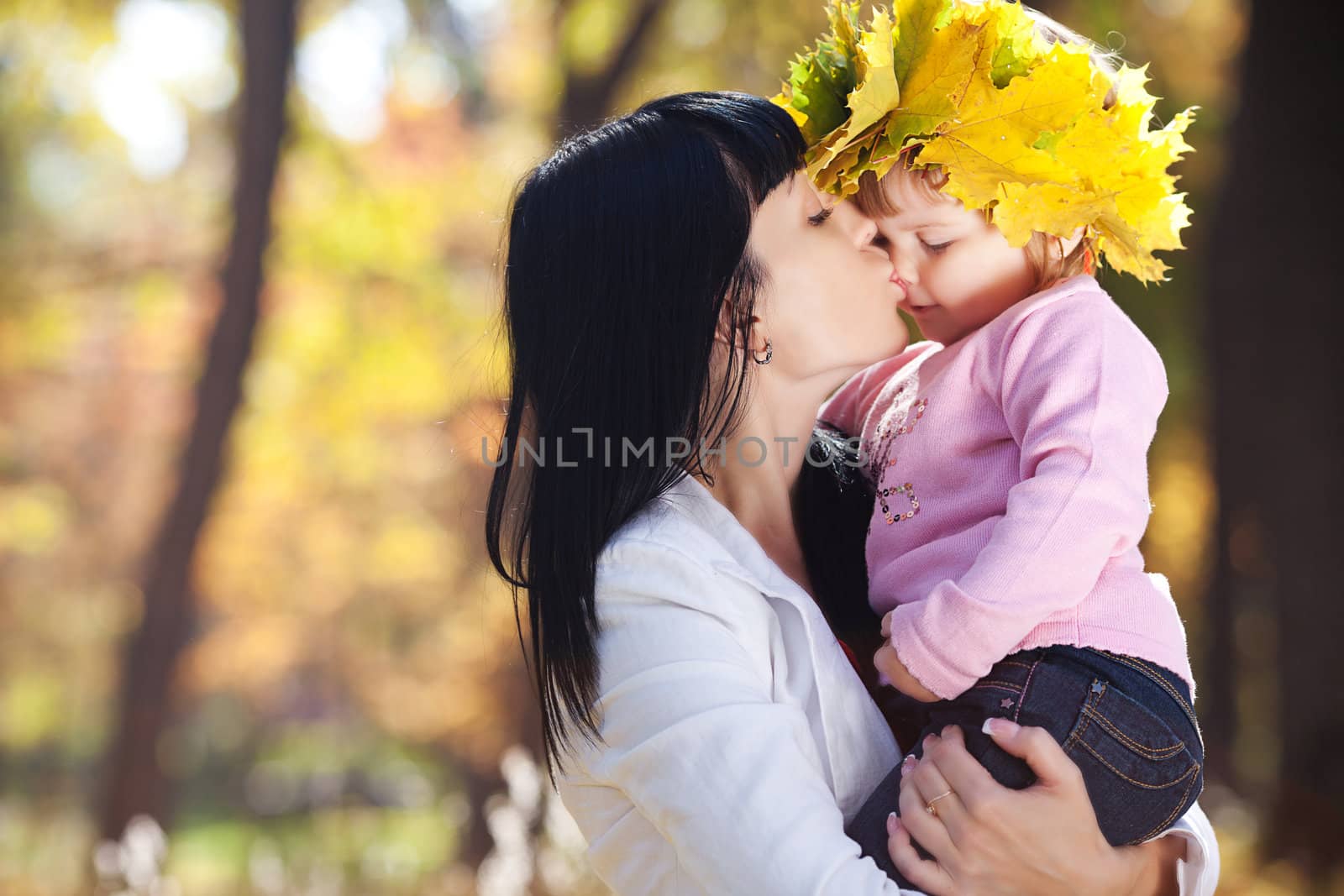 beautiful young mother kissing her daughter in autumn forest