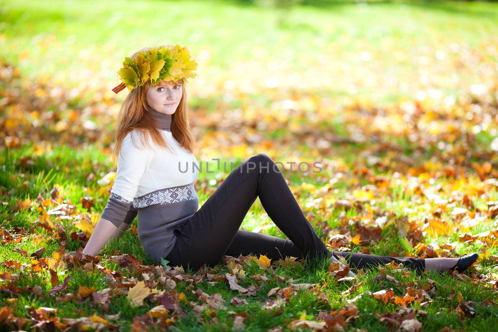 young redhead teenager woman in a wreath of maple leaves sitting on the grass