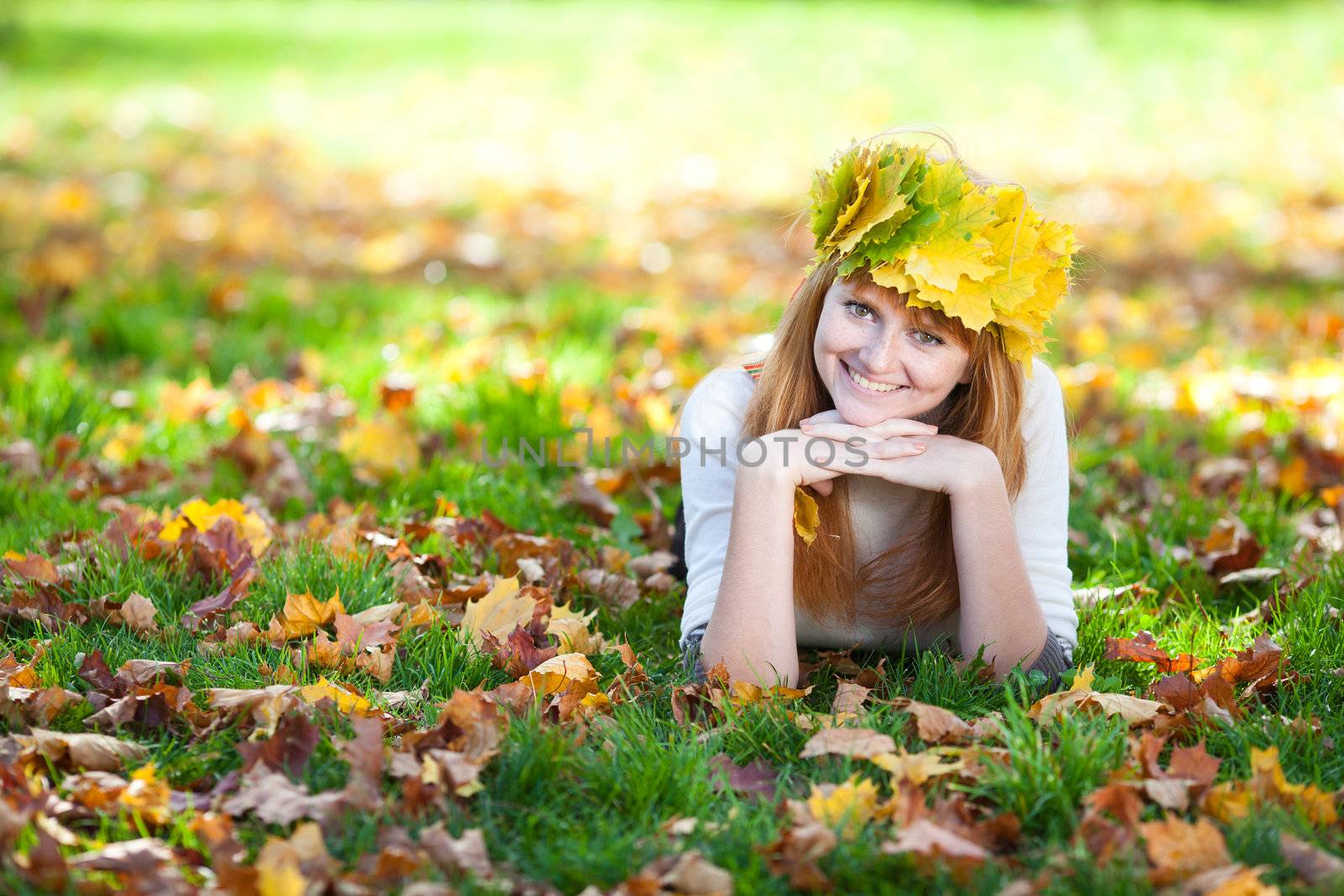 young redhead teenager woman in a wreath of maple leaves lying on the grass