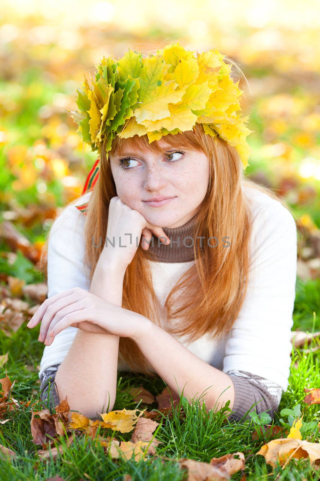 young redhead teenager woman in a wreath of maple leaves lying on the grass