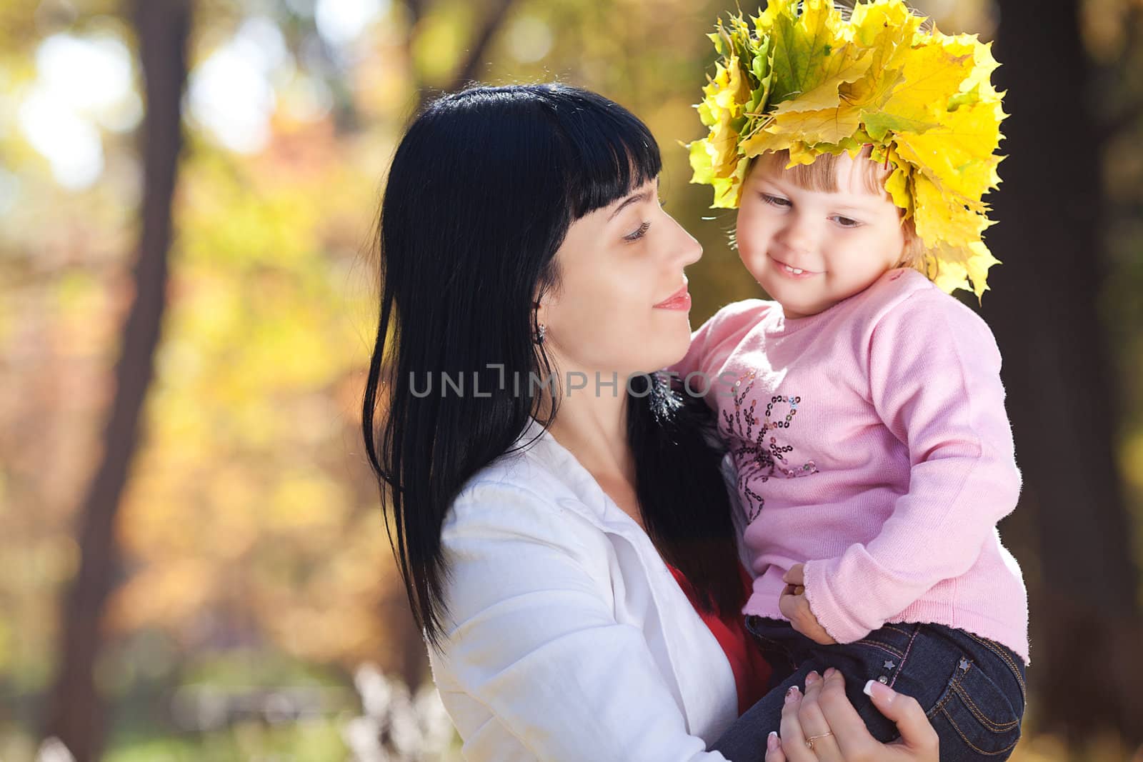 beautiful young mother holding her daughter in a wreath of maple leaves 