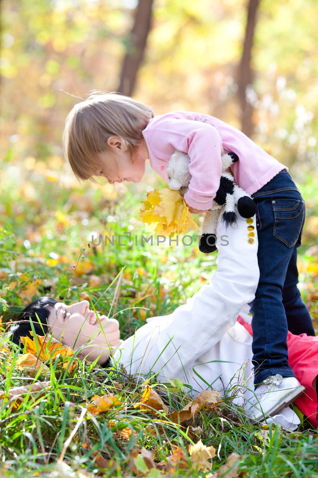 beautiful young mother and her daughter lying on the autumn leaves