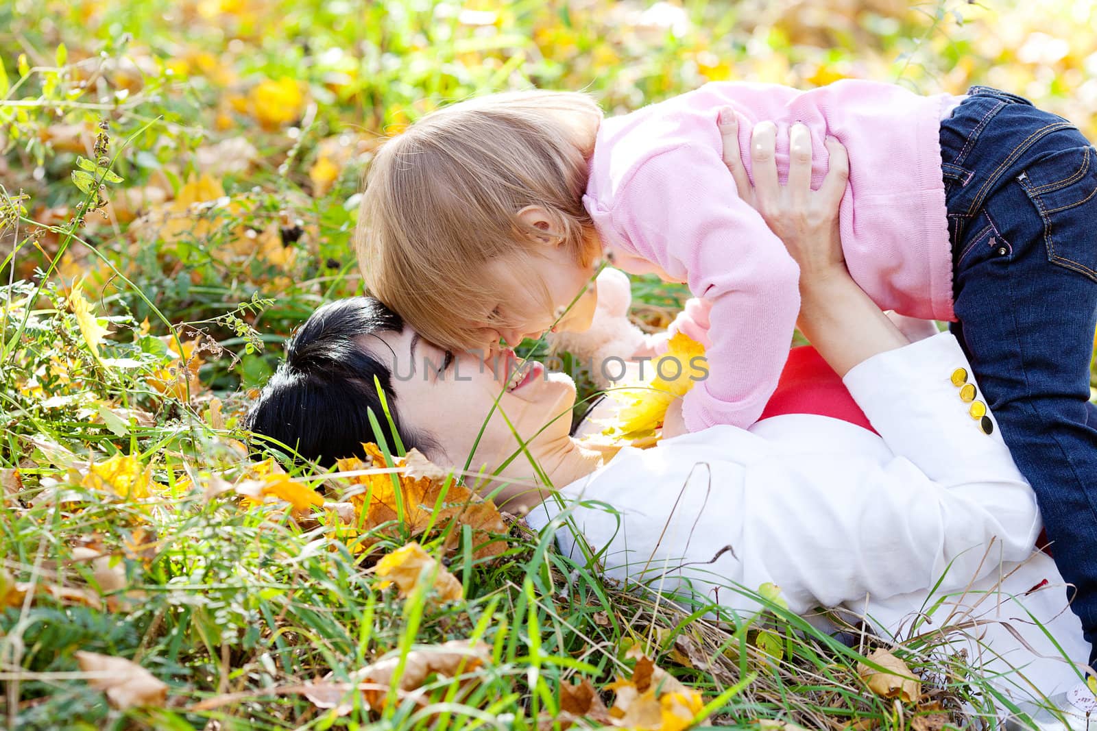 beautiful young mother and her daughter lying on the autumn leaves