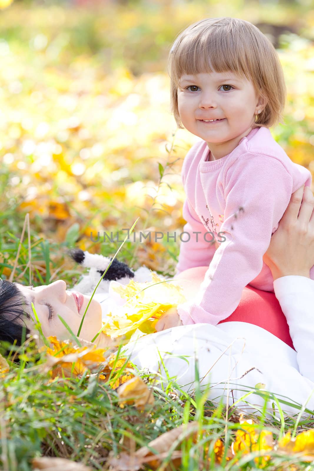 beautiful young mother and her daughter lying on the autumn leaves