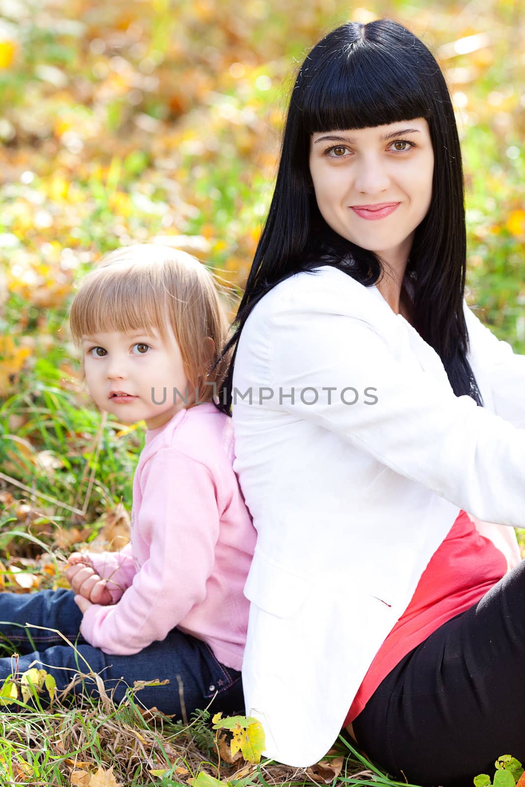 beautiful young mother and her daughter sitting on the autumn leaves