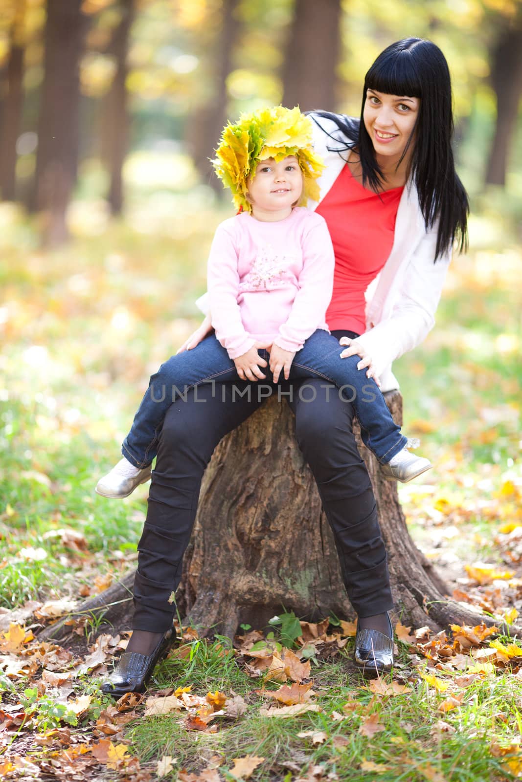 beautiful young mother holding her daughter in a wreath of maple leaves 