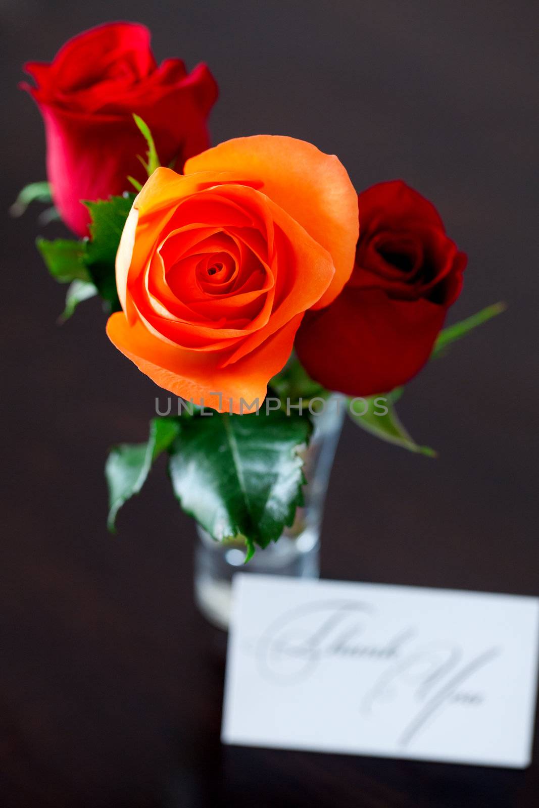 bouquet of colorful roses in a vase and card with the words thank you on a wooden table