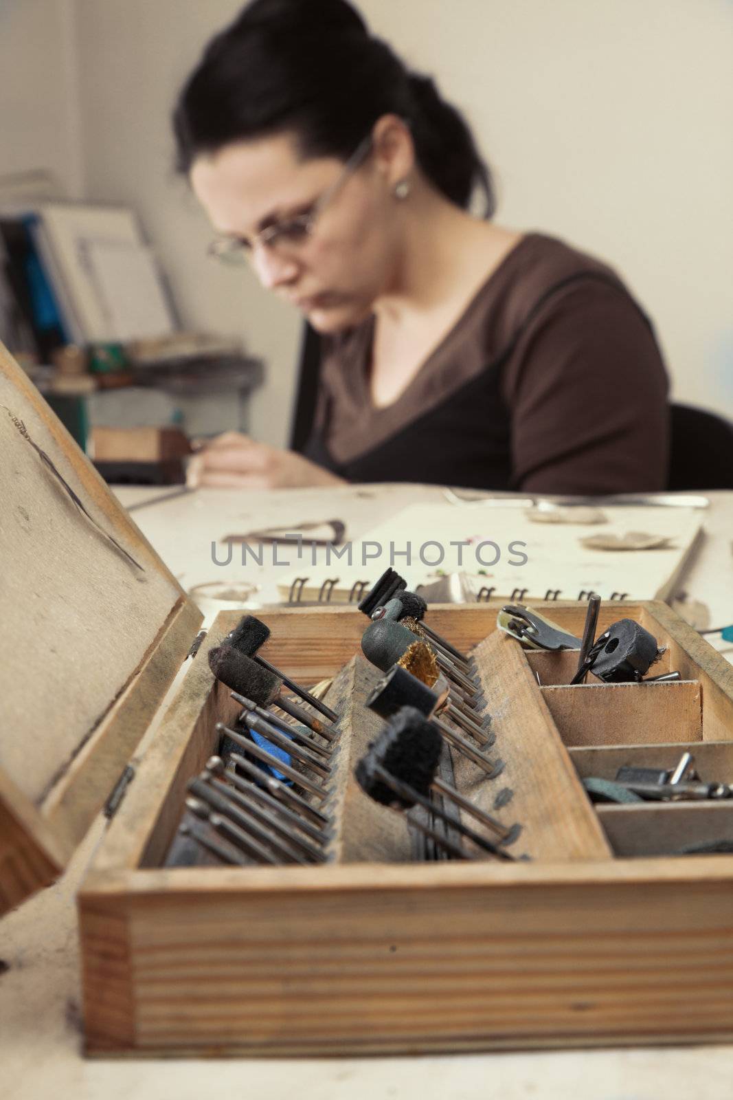 Selective focus on the opened wooden toolbox , in front of a femeale jeweler working in her workshop.