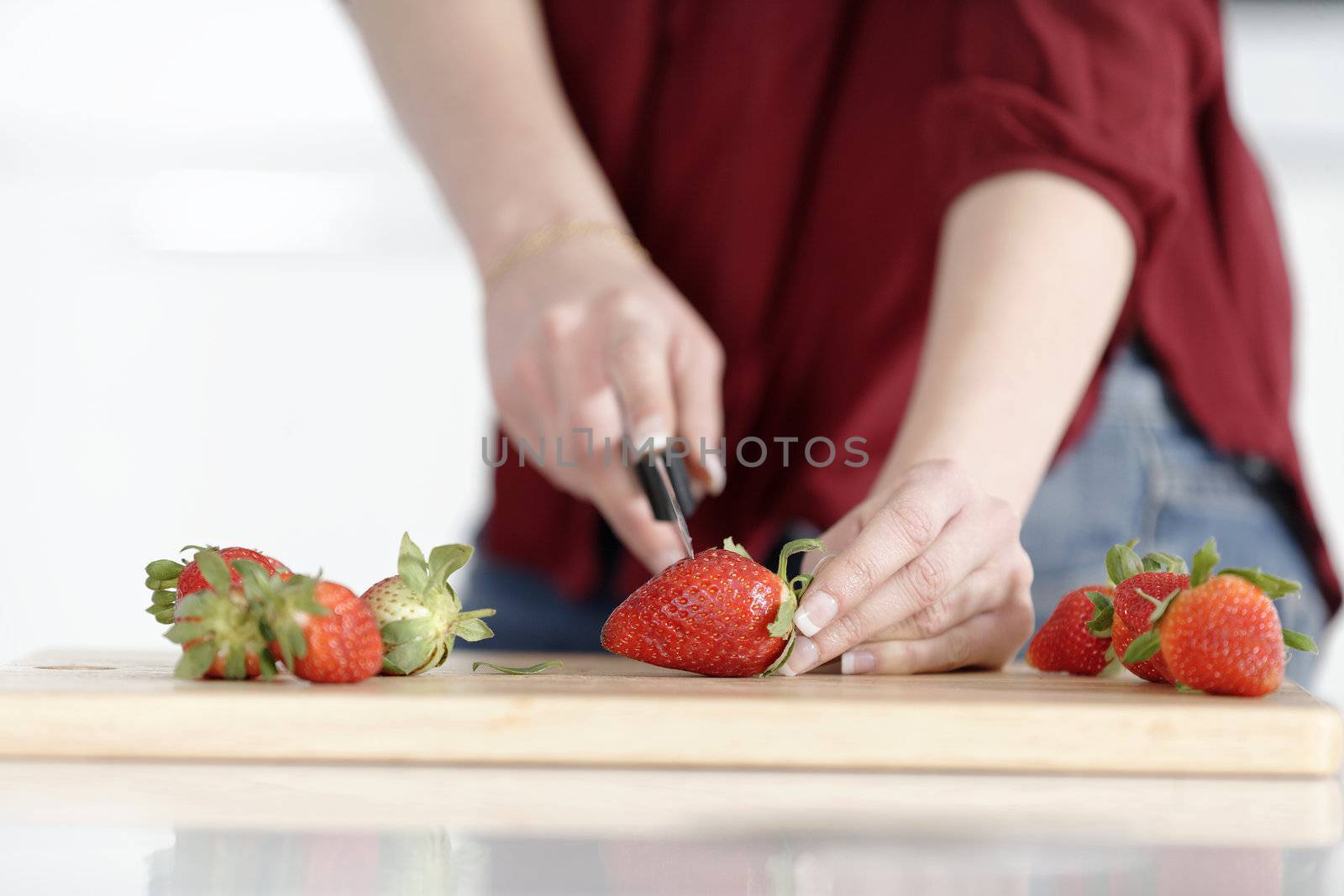 Beautiful young woman preparing strawberries in her white kitchen