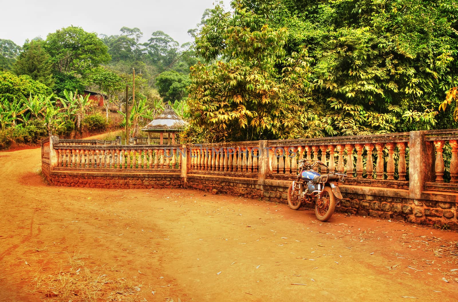Old motorcycle against fence, African dirt road landscape