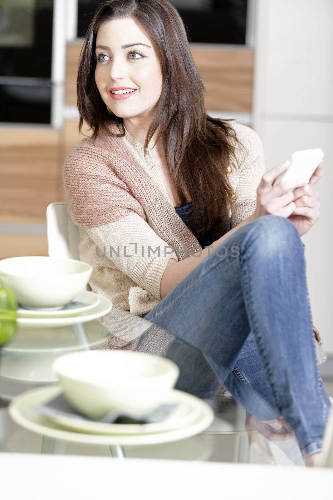 Beautiful young woman chatting on her mobile phone in her kitchen