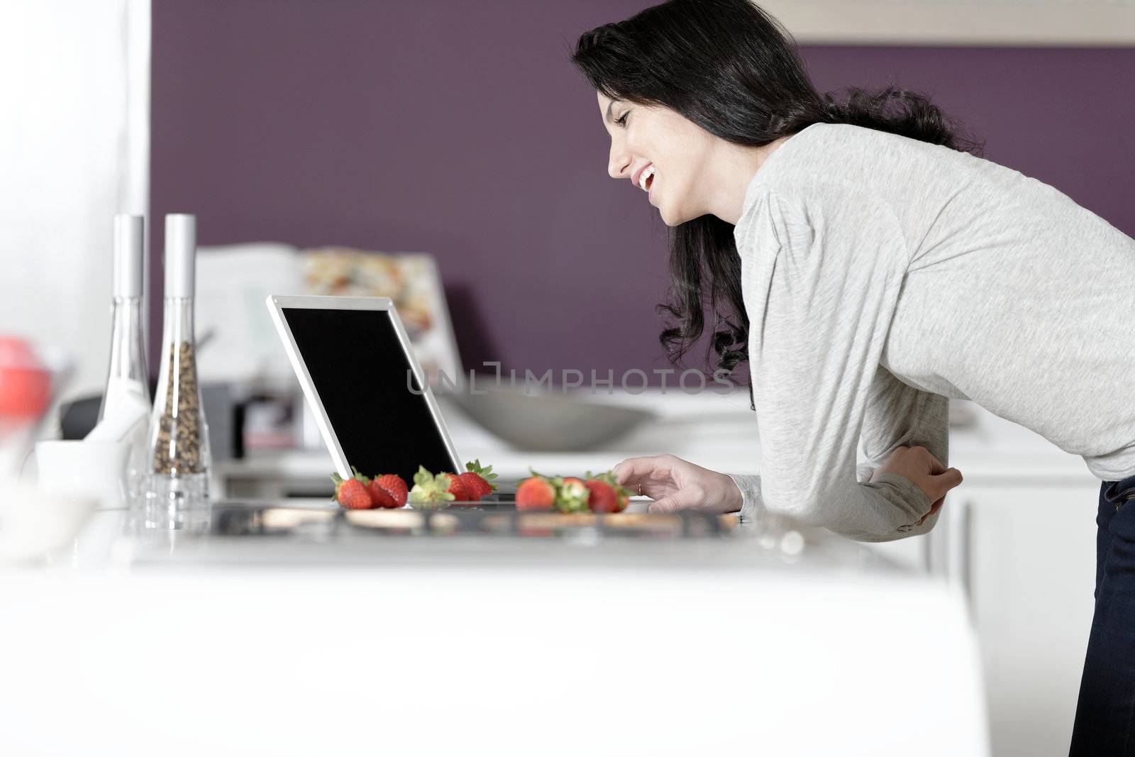 Beautiful young woman reading a recipe from a laptop in her kitchen