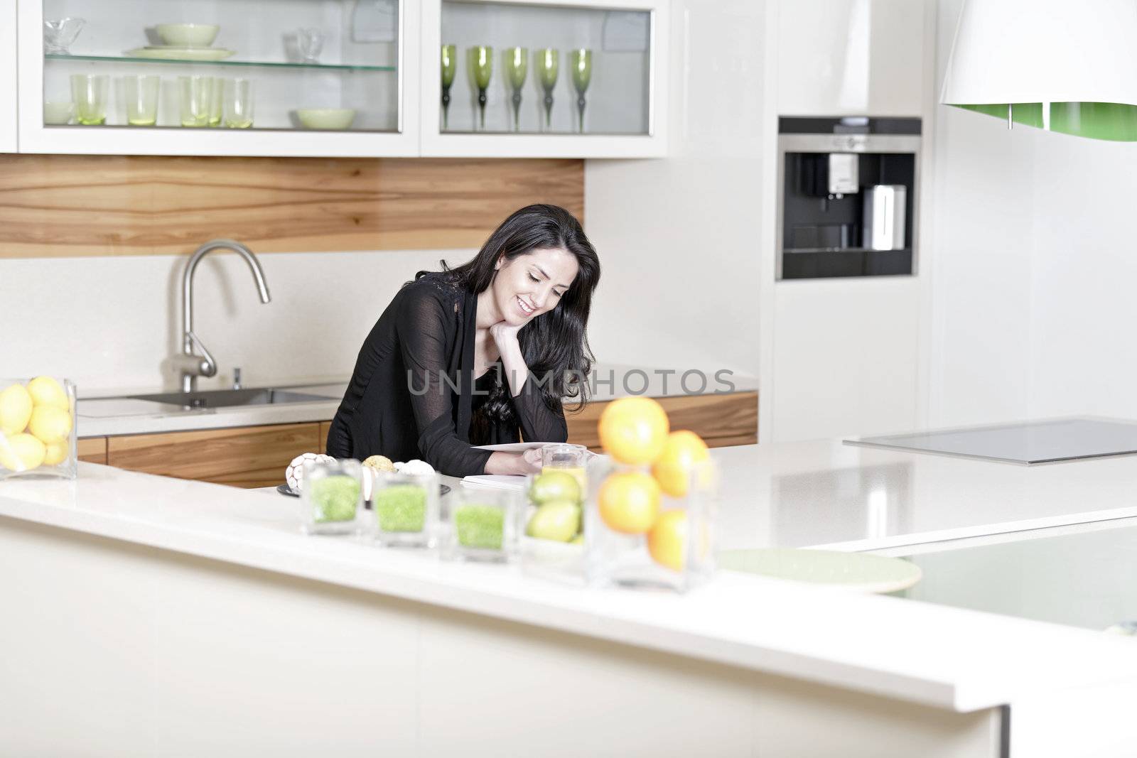 Beautiful young woman reading from a recipe book in her kitchen