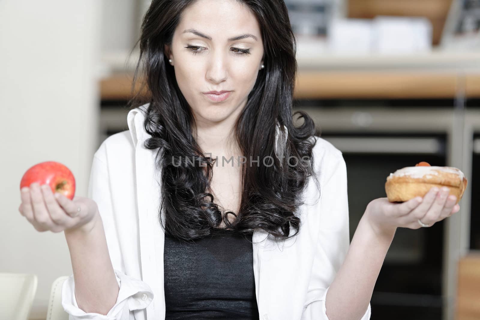 Attractive young woman choosing between a sticky cake or fresh fruit.