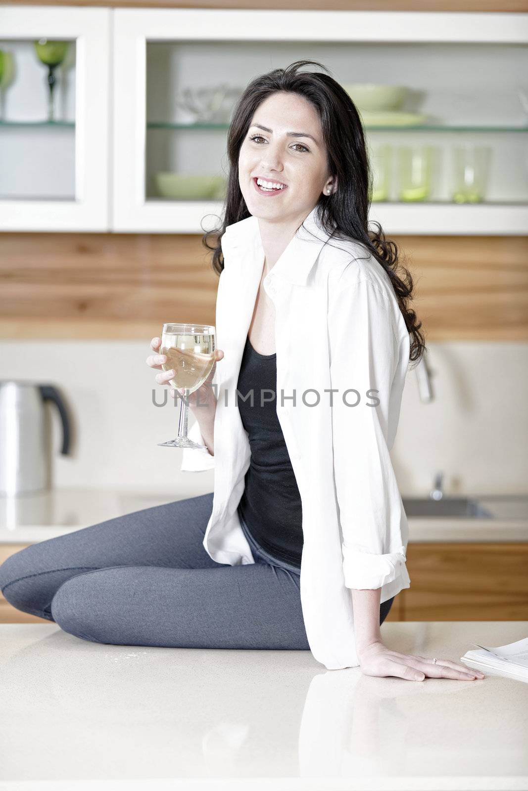 Beautiful young woman enjoying a glass of wine in her kitchen.