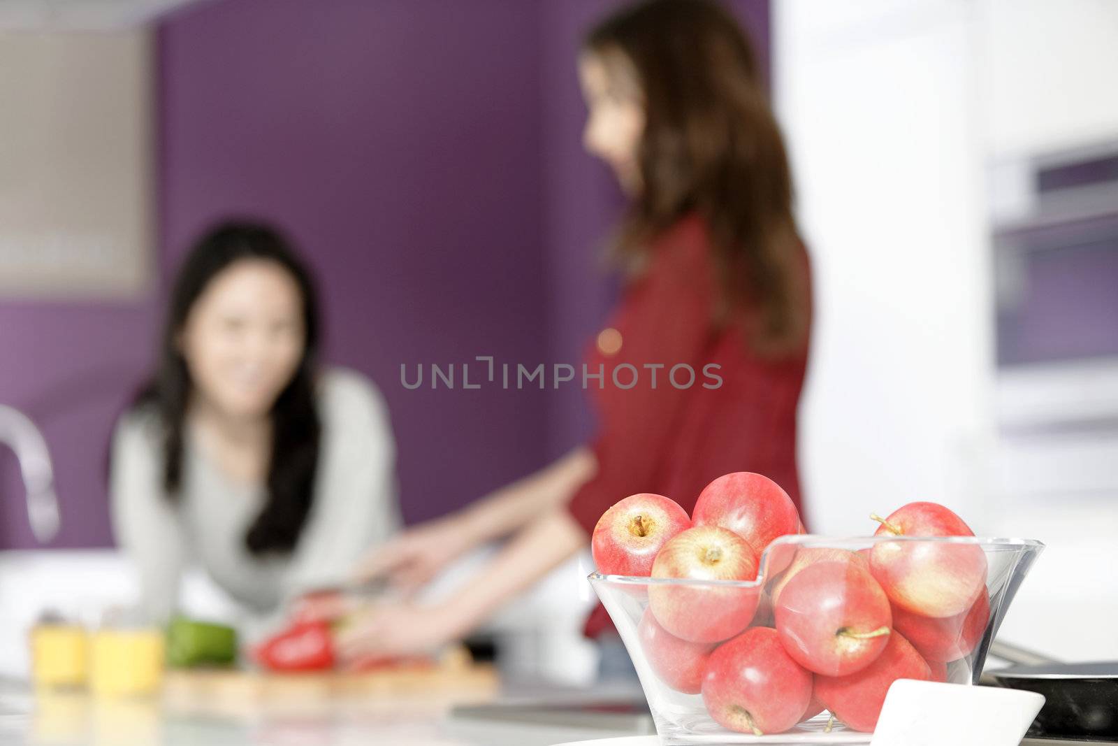 Two attractive young women preparing food in a white kitchen while talking.