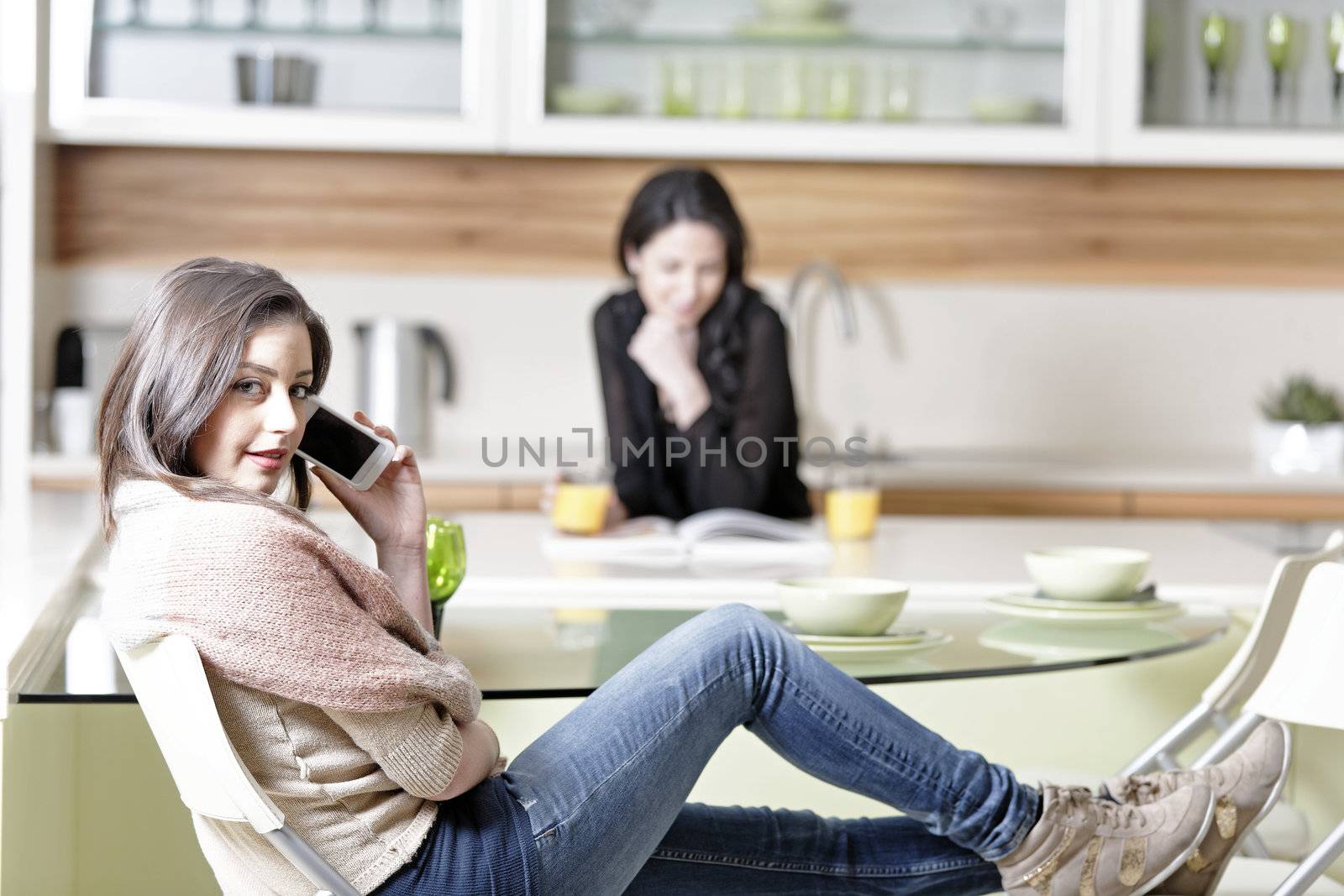 Two friends in a kitchen relaxing on the phone and reading