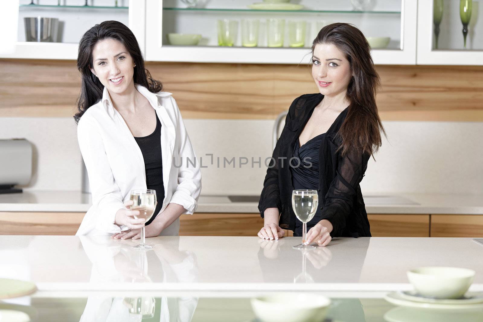 Two friends in a kitchen catching up and having a glass of wine.