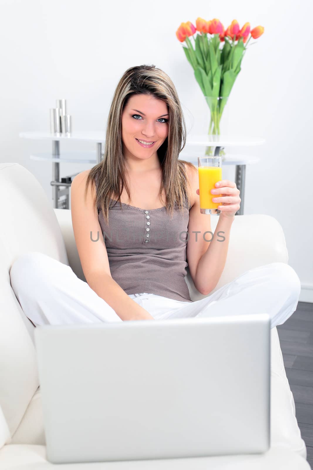 young woman at home on sofa with computer and orange juice