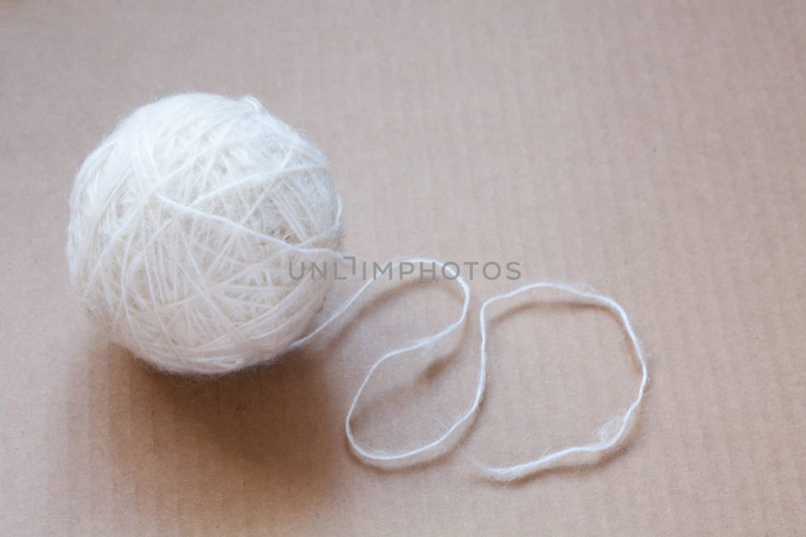 Ball of white wool yarn on cardboard background by sfinks