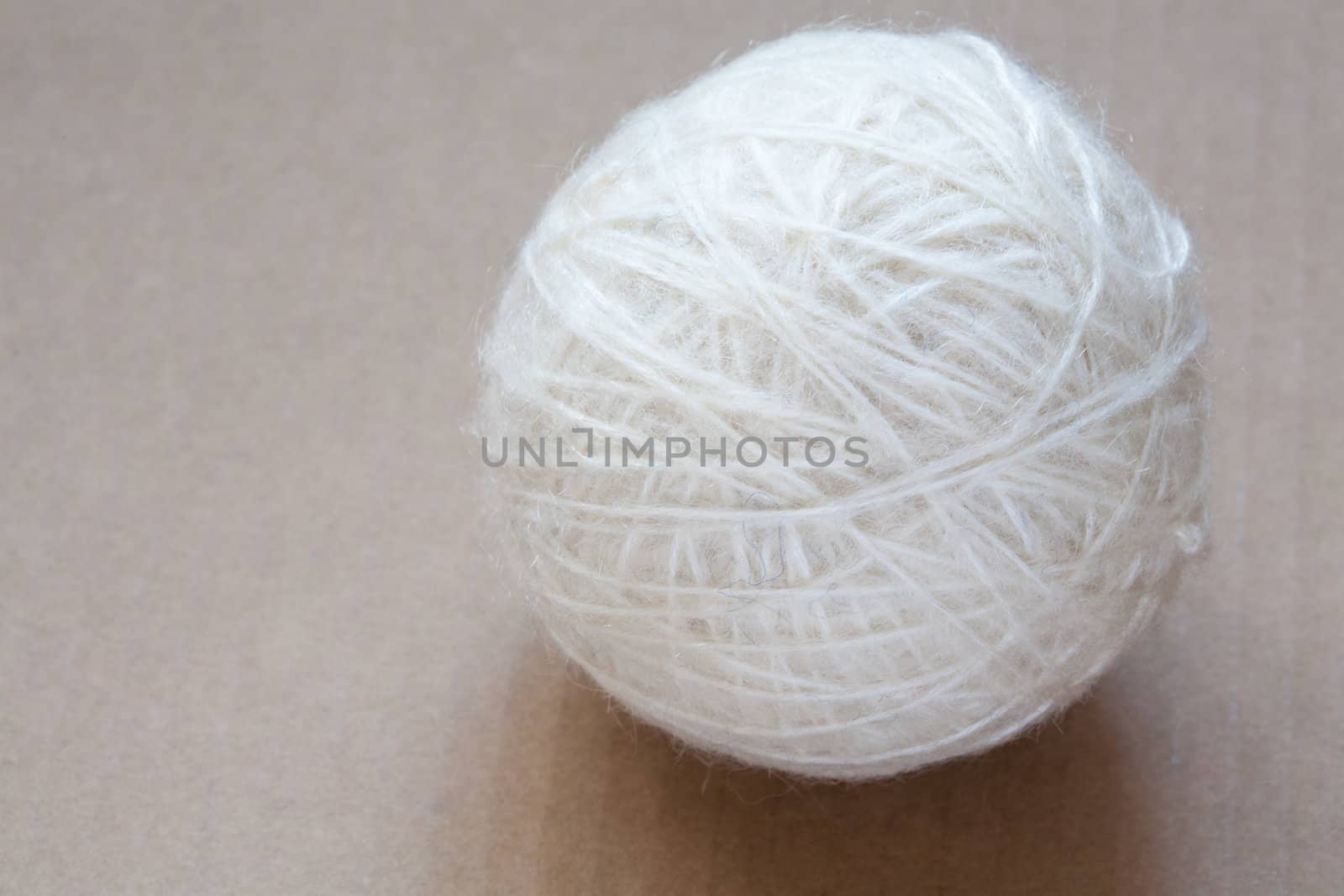 Ball of white wool yarn on cardboard background by sfinks