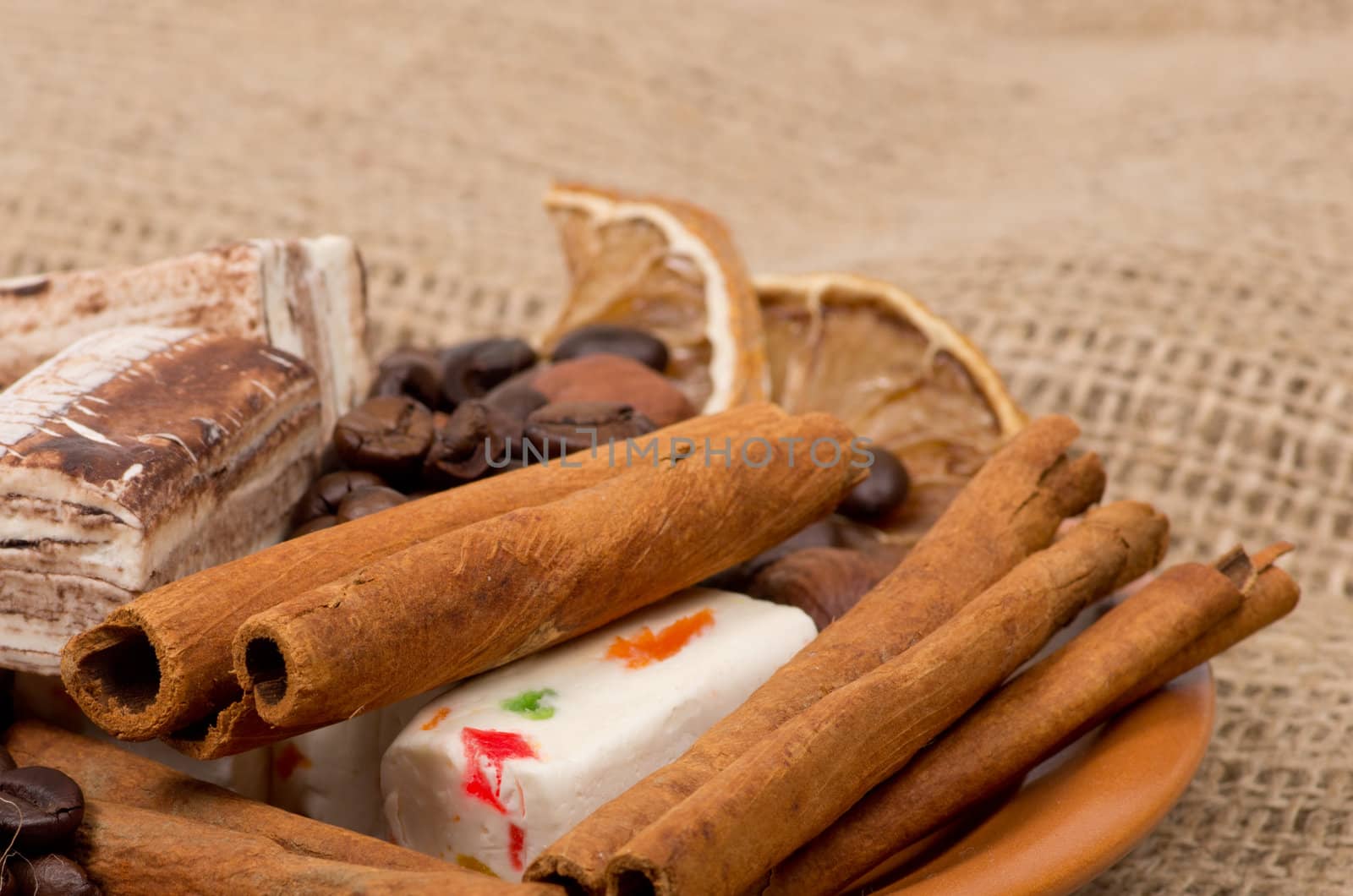 Sweets, cinnamon, nuts and coffee beans on a saucer, on burlap background.