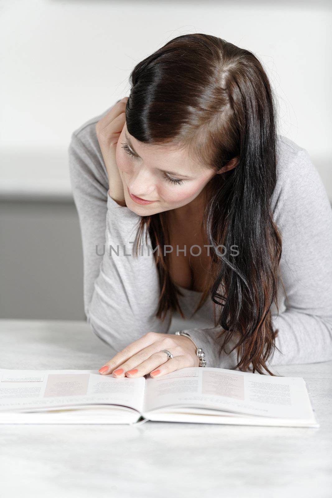 Beautiful young woman reading from a cookery book in her kitchen.