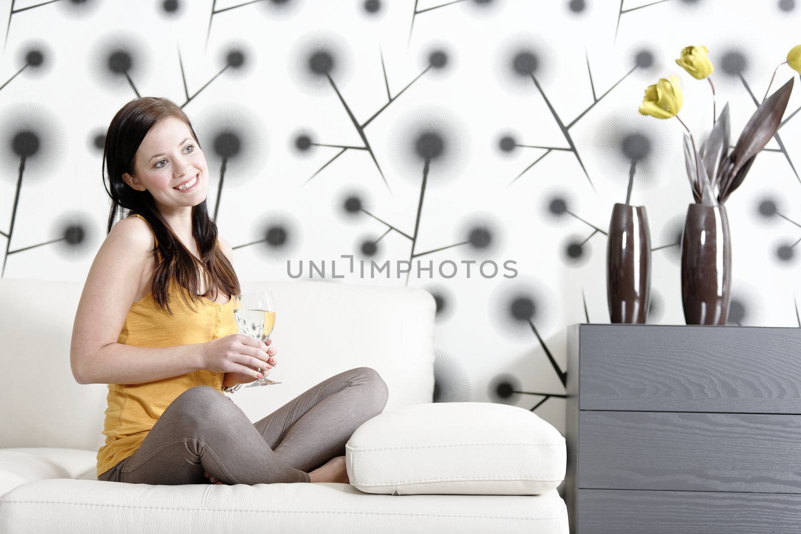 Attractive young woman relaxing on her sofa at home with a glass of white wine.