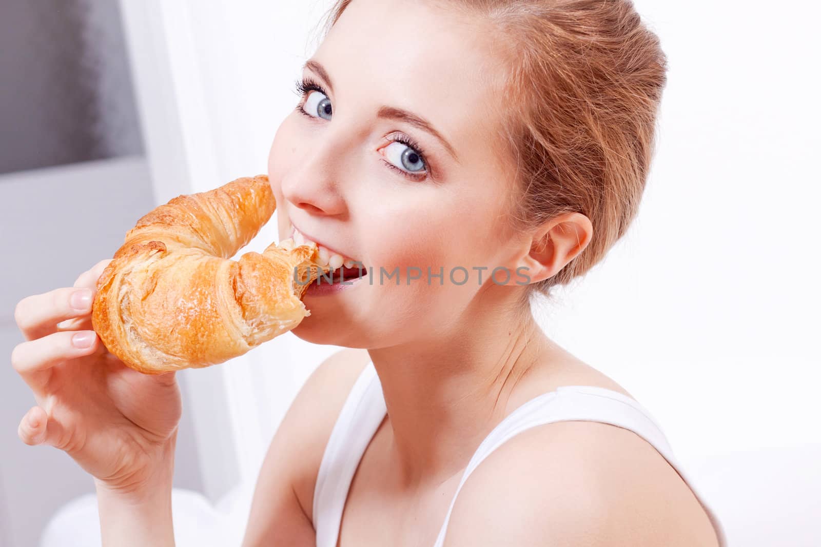 attractive smiling young woman eating croissant for breakfast 
