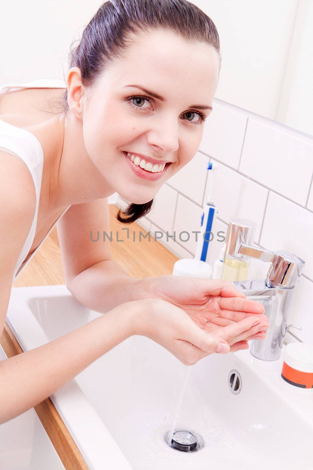 attractive smiling woman washing face with clear water in bathroom