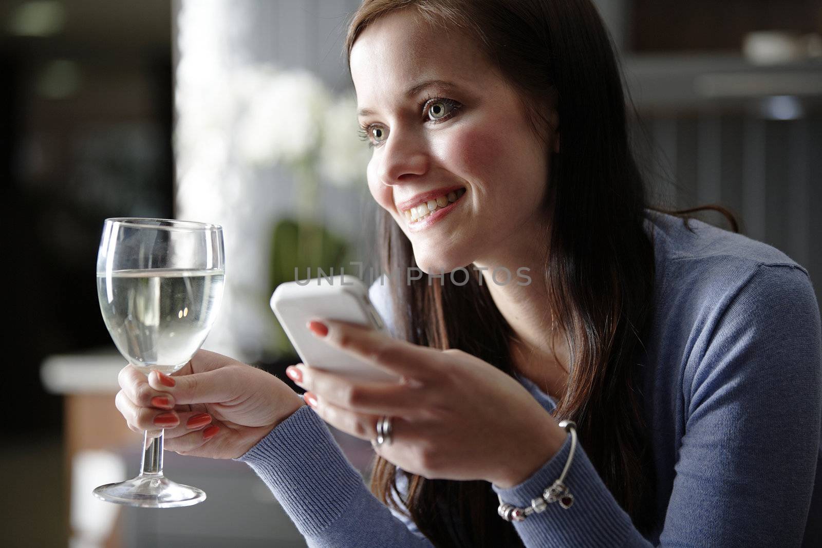 Attractive young woman enjoying a glass of wine in her kitchen while chatting on the phone.