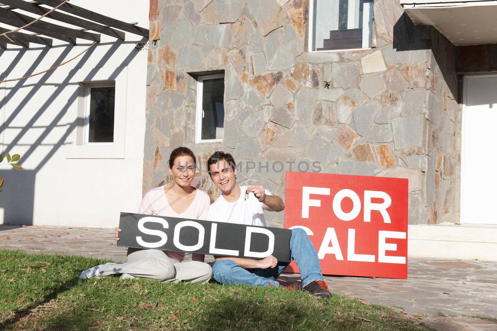 Couple holding sold sign and keys against their new house
