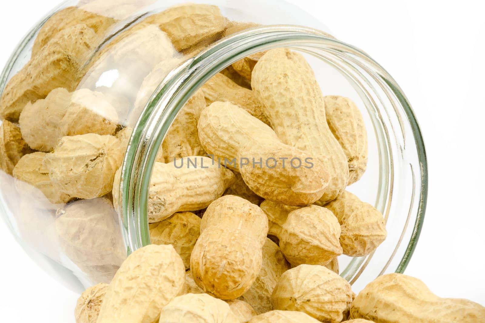 Close up of a glass jar full of unpeeled peanuts on a white background