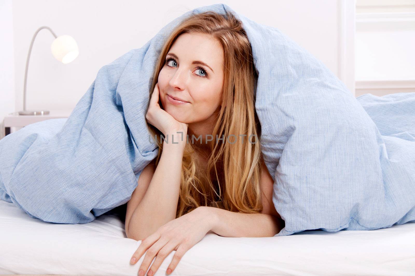 cute smiling blonde woman in the morning under blanket