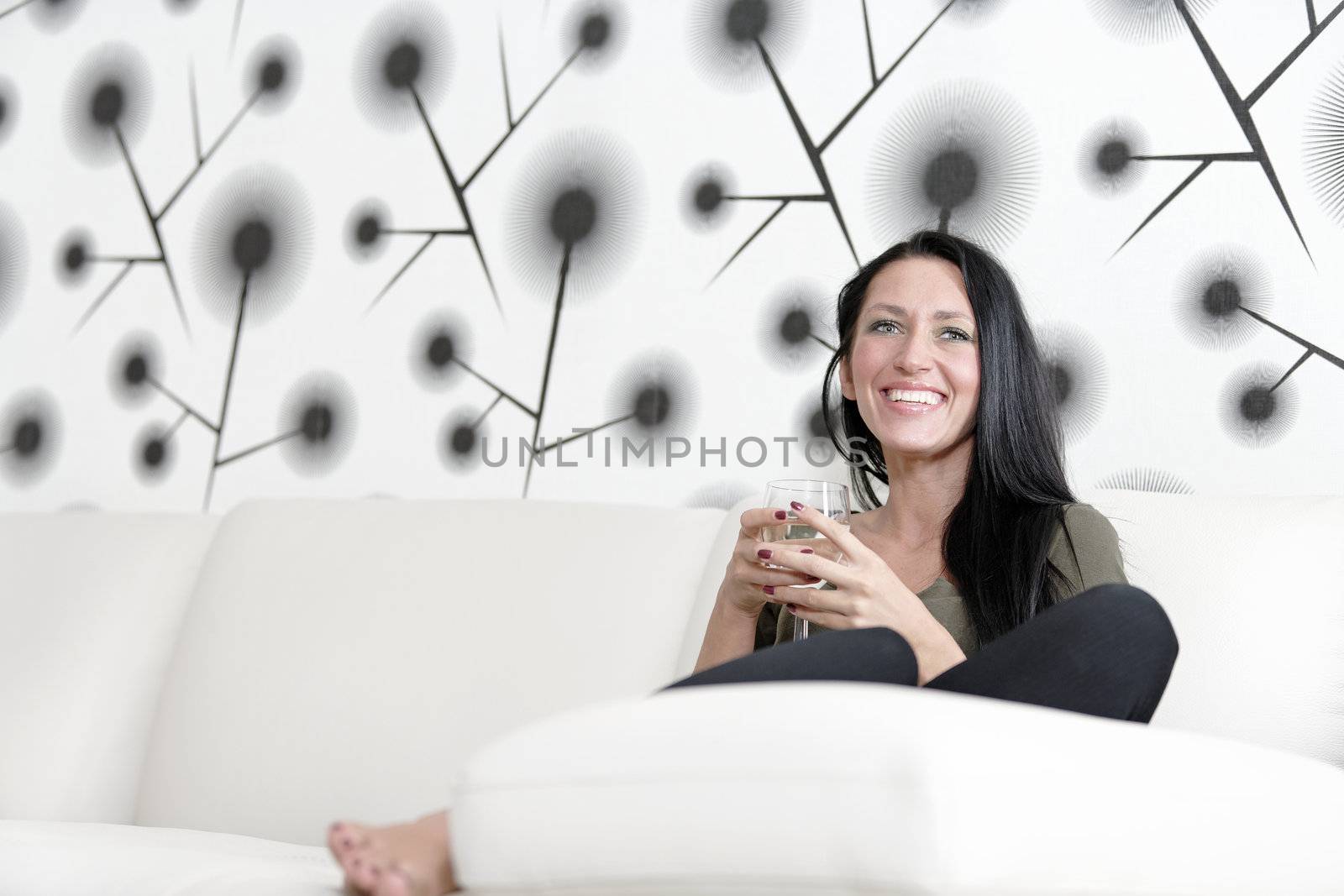 Attractive young woman relaxing on her sofa at home with a glass of white wine.