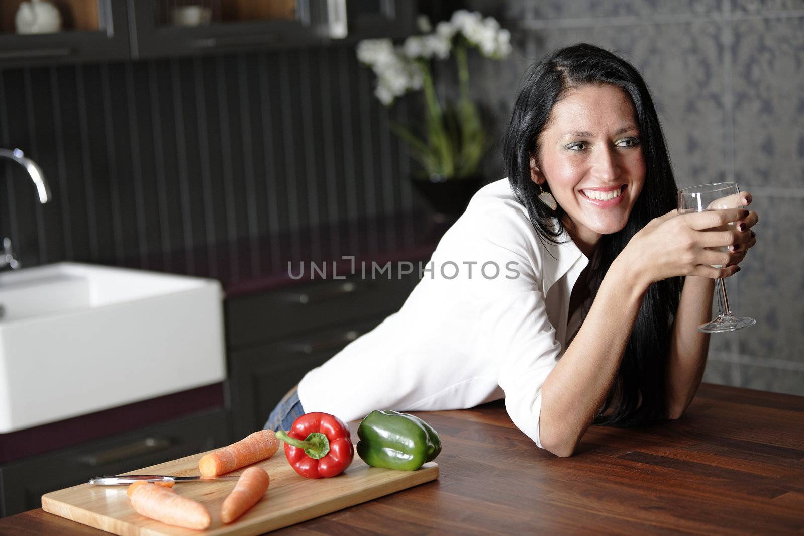 Attractive young woman enjoying a glass of wine in her kitchen.