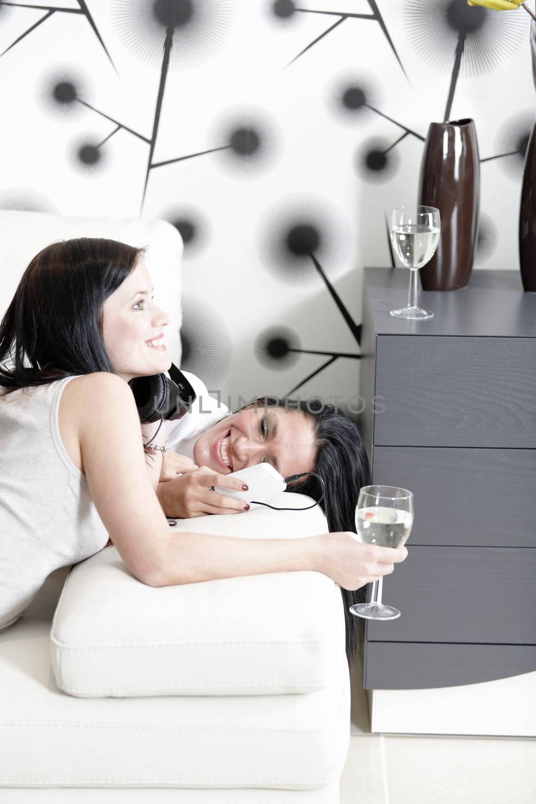 Two beautiful young woman listening to music on headphones at home on the sofa.