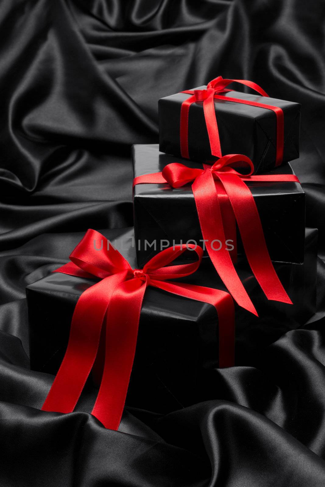 Black gift boxe with red satin ribbons and bows, over black satin