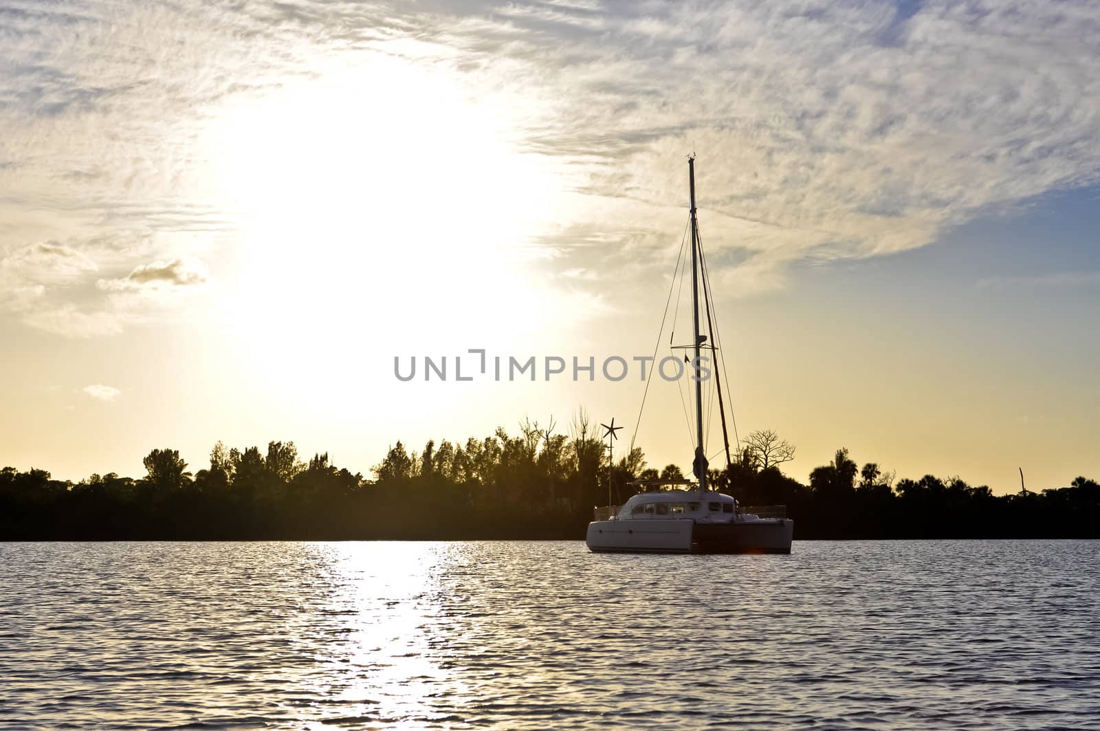 Catamaran sailboat anchored in harbor at sunset