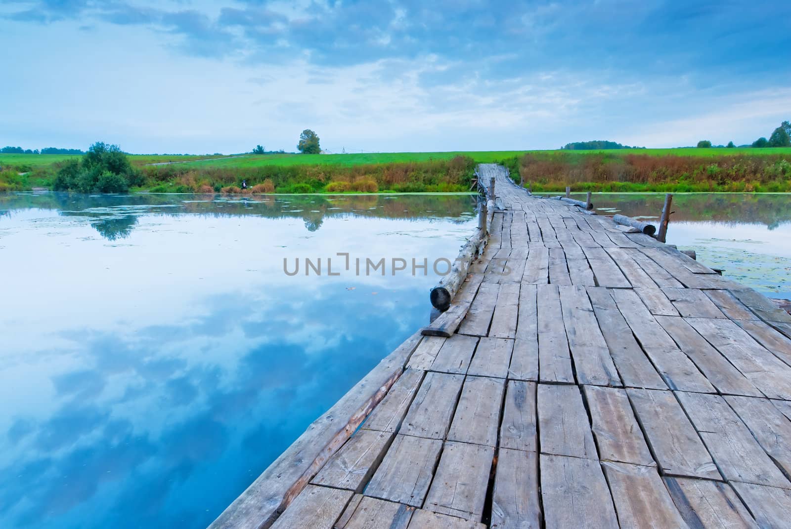 wooden bridge over a small lake in the early morning by kosmsos111