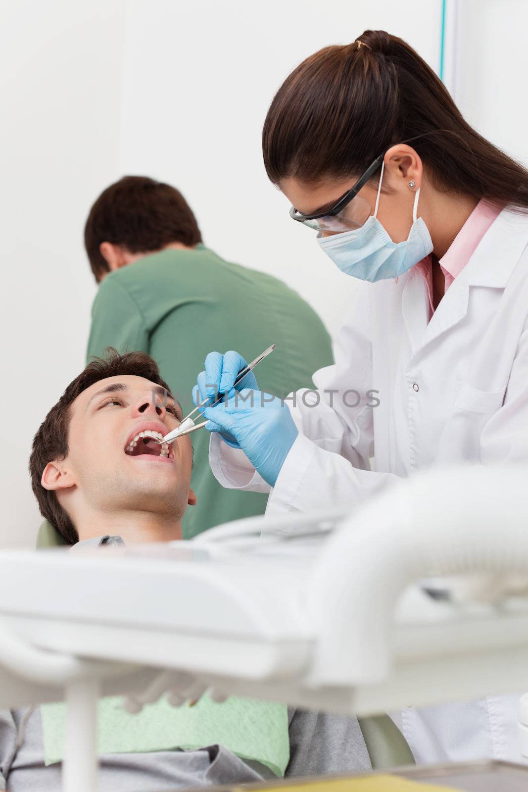 Young female dentist working on patient's teeth with assistant in the background