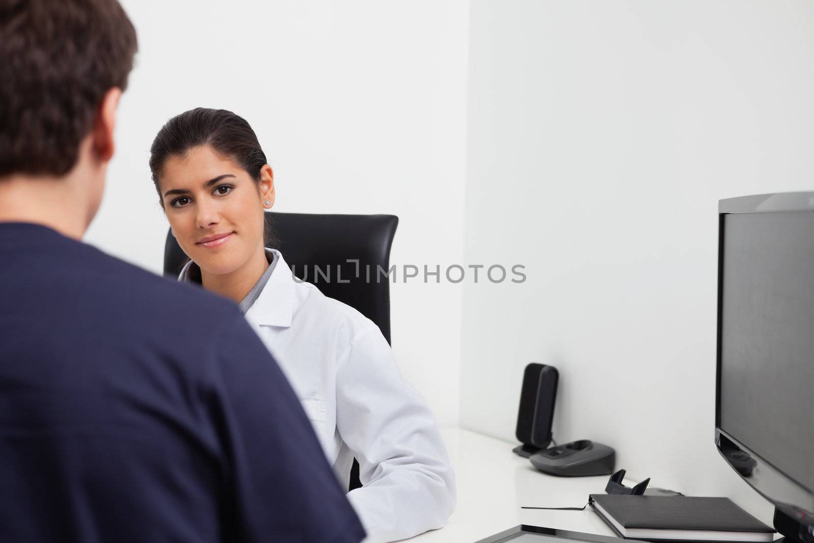 Female dentist sitting at her desk in front of patient at clinic