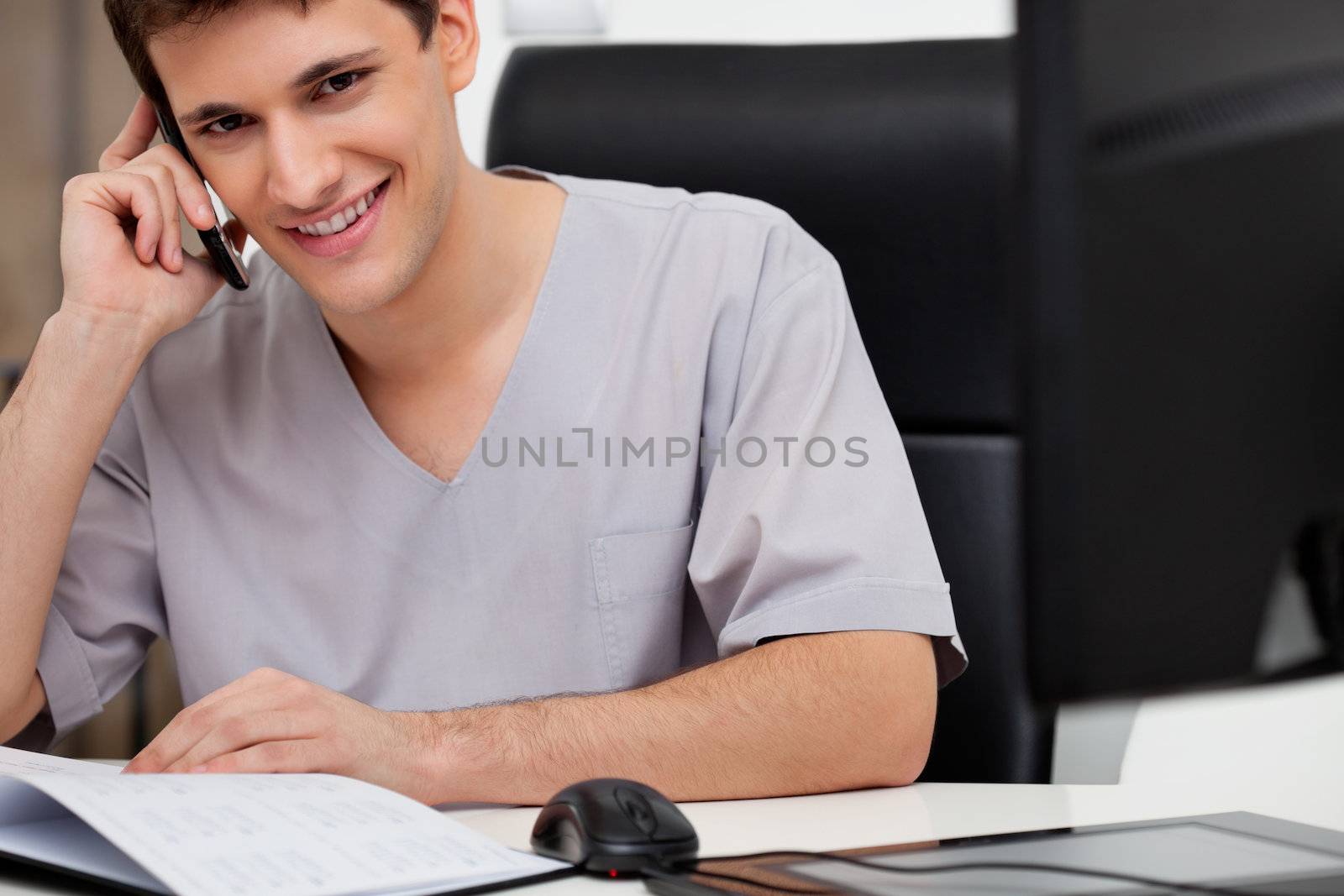 Happy male doctor talking on mobile phone at his desk