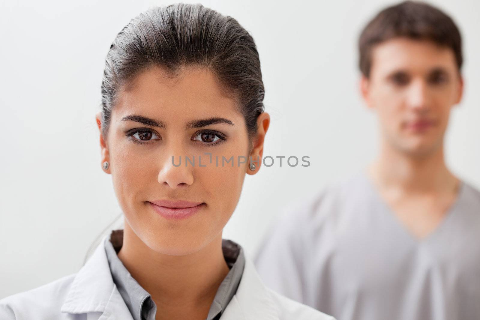 Portrait of pretty female doctor with practitioner standing in background