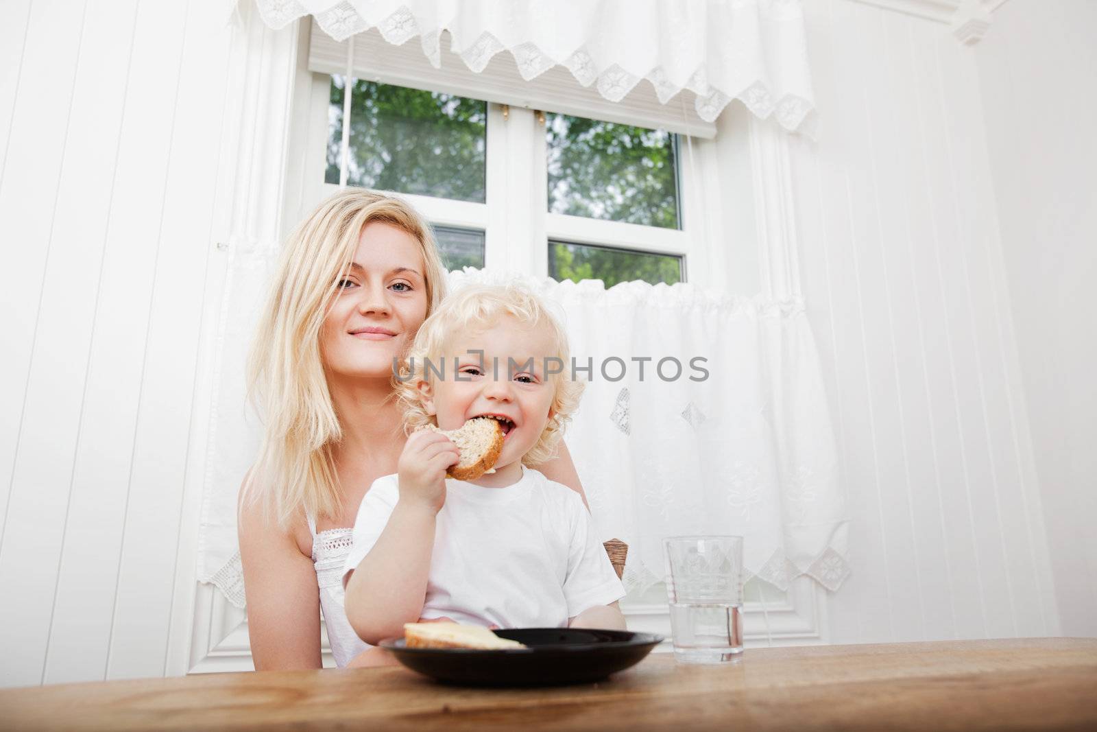 Portrait of cute little boy eating bread with mother at home