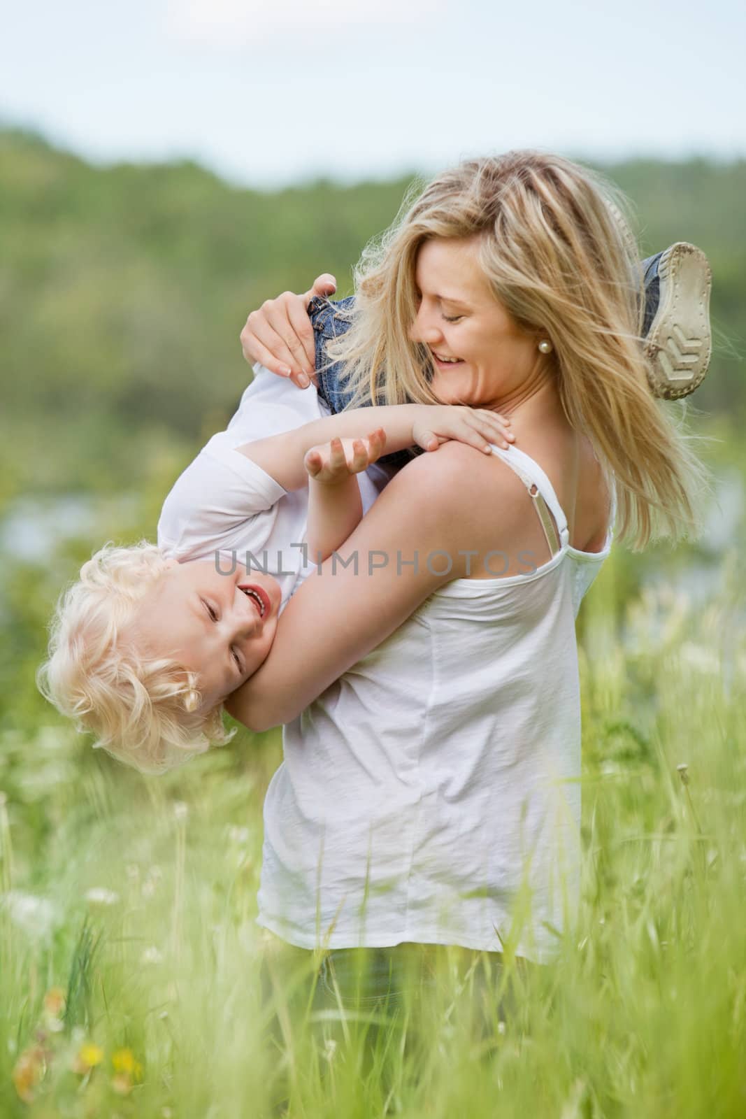 An attractive young woman playing with sweet little boy in green meadow